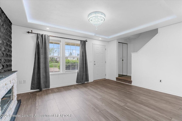 unfurnished living room with wood finished floors, baseboards, a chandelier, a tray ceiling, and recessed lighting