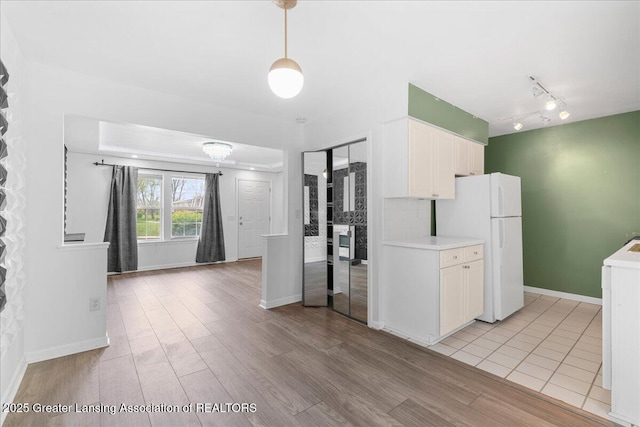 kitchen with light wood-type flooring, freestanding refrigerator, white cabinetry, and light countertops
