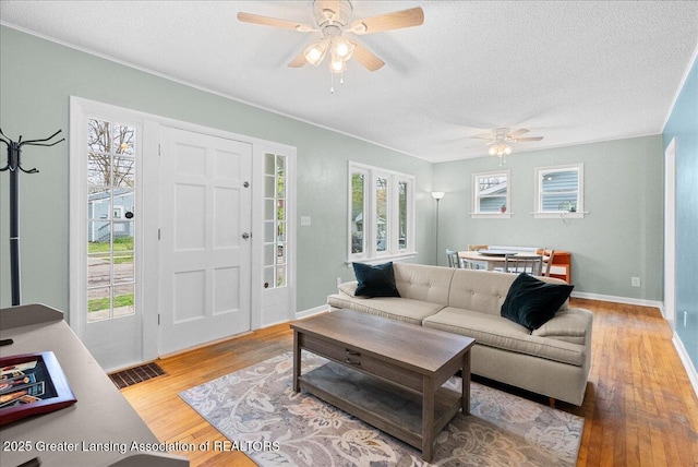 living area featuring a ceiling fan, a textured ceiling, visible vents, and wood finished floors