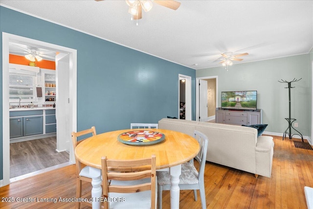 dining room with ceiling fan, ornamental molding, wood finished floors, and visible vents