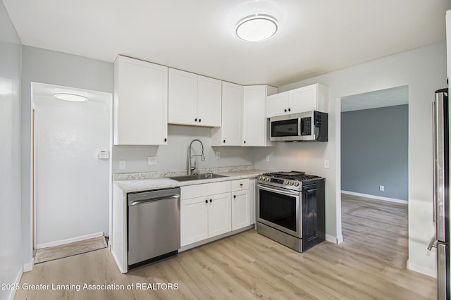 kitchen with a sink, appliances with stainless steel finishes, white cabinets, and light wood-style flooring