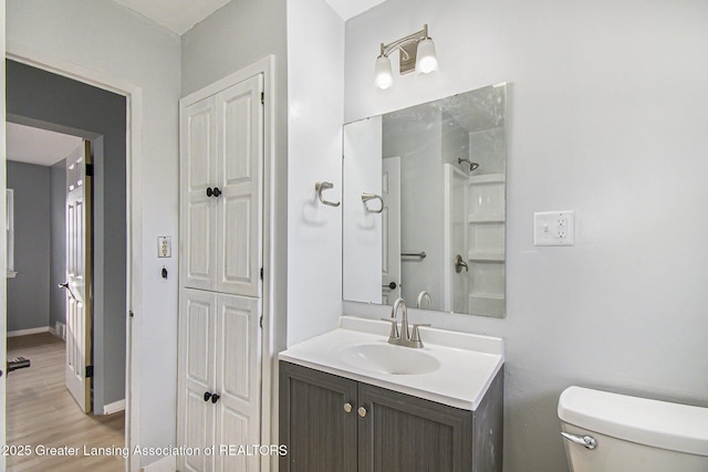 bathroom featuring toilet, baseboards, wood finished floors, and vanity