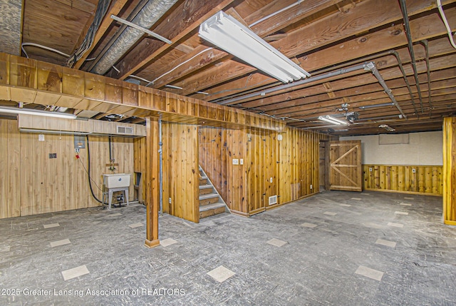 unfinished basement with wood walls, visible vents, a sink, and stairway