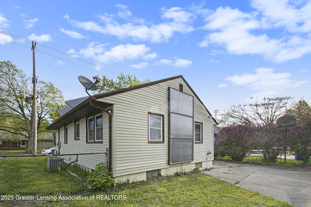 view of side of home with a lawn, central AC, and fence