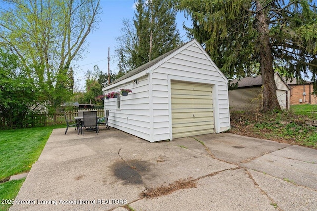 detached garage featuring concrete driveway and fence