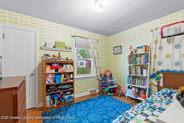bedroom featuring visible vents, baseboards, wallpapered walls, and wood finished floors