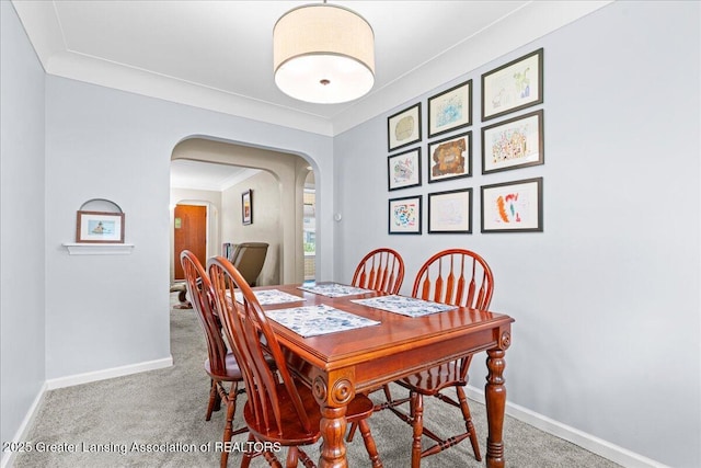 carpeted dining space with ornamental molding, baseboards, and arched walkways