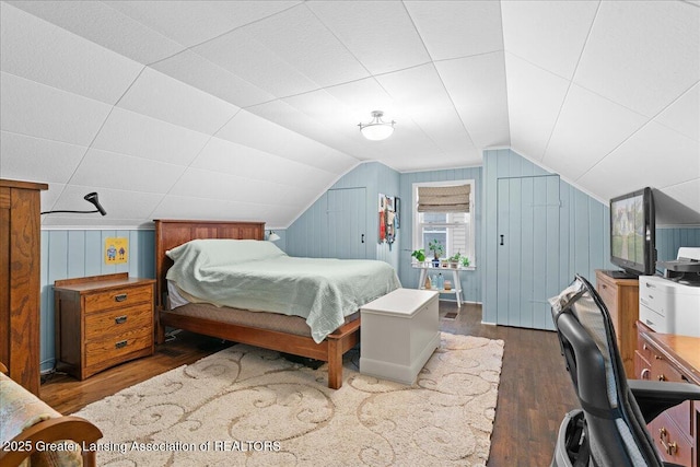 bedroom with vaulted ceiling, wooden walls, and wood finished floors