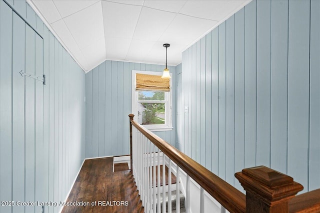 corridor featuring vaulted ceiling, dark wood-style flooring, wooden walls, and an upstairs landing
