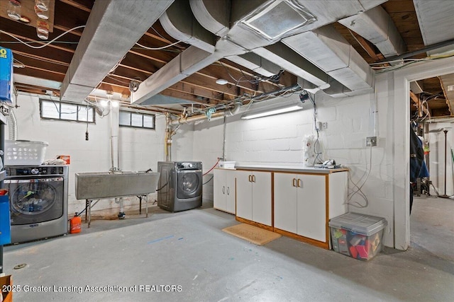 basement featuring washer and clothes dryer, a sink, and concrete block wall