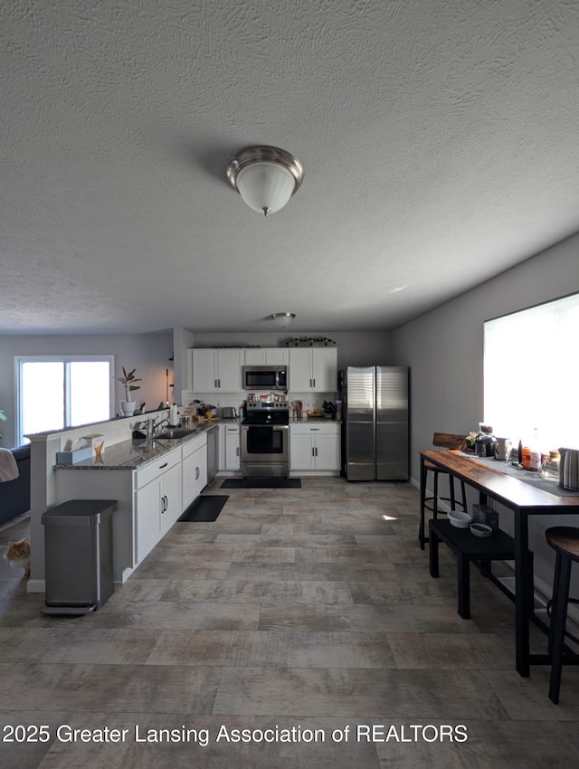 850 Saint Johns Chase, Grand Ledge, MI 48837 - kitchen with appliances with stainless steel finishes, a peninsula, white cabinetry, a textured ceiling, and dark stone countertops