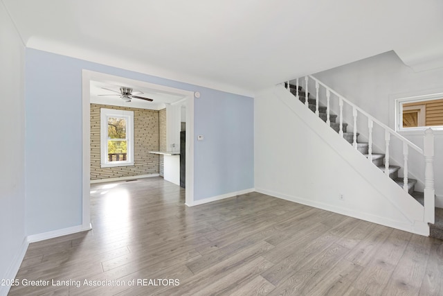 unfurnished living room with baseboards, stairs, a ceiling fan, and wood finished floors