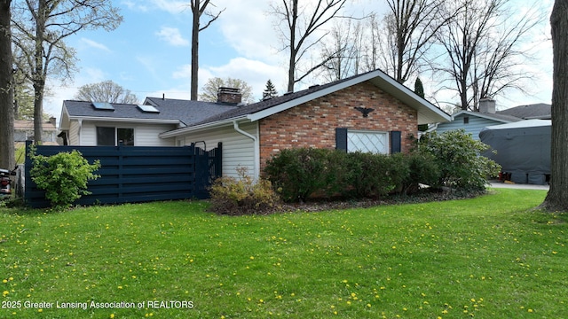 view of side of property with a yard, fence, a chimney, and brick siding