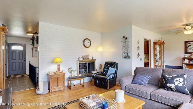 living area featuring a fireplace, light wood-style flooring, and a ceiling fan