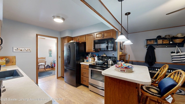 kitchen with hanging light fixtures, a breakfast bar, black appliances, light countertops, and light wood-style floors