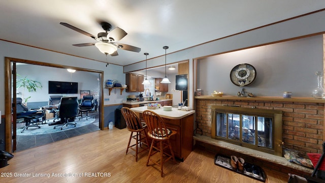 kitchen with a peninsula, light wood finished floors, a ceiling fan, a sink, and light countertops