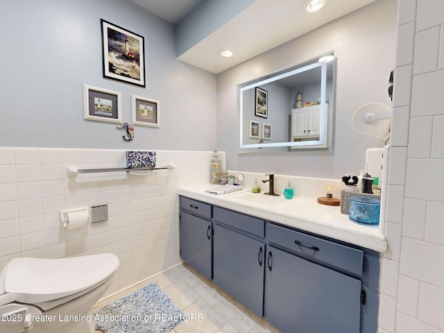 bathroom with tile walls, toilet, tile patterned floors, vanity, and a wainscoted wall