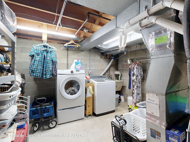 washroom featuring washing machine and clothes dryer, a sink, laundry area, and concrete block wall