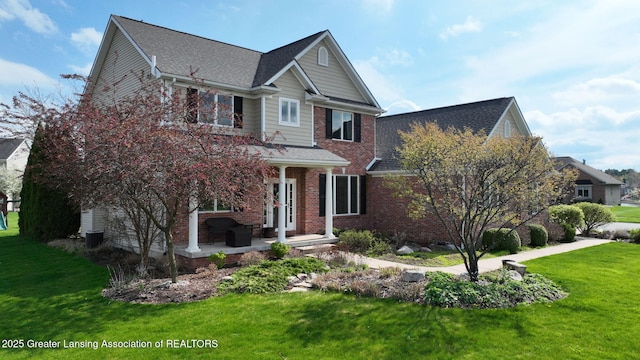 traditional-style home featuring a patio area, a shingled roof, brick siding, and a front lawn