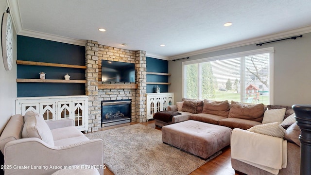 living room featuring wood finished floors, crown molding, a stone fireplace, built in shelves, and recessed lighting