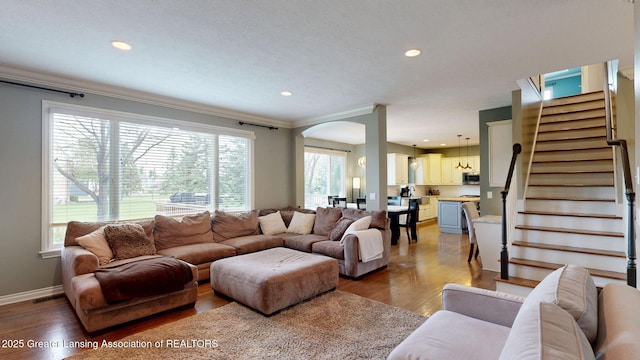 living area with stairway, ornamental molding, arched walkways, and wood finished floors