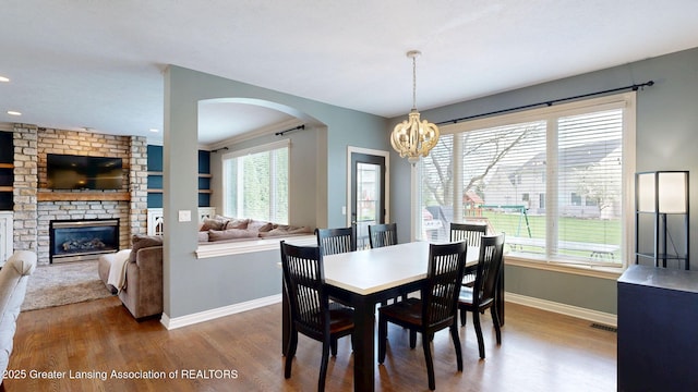 dining space featuring baseboards, an inviting chandelier, wood finished floors, and arched walkways