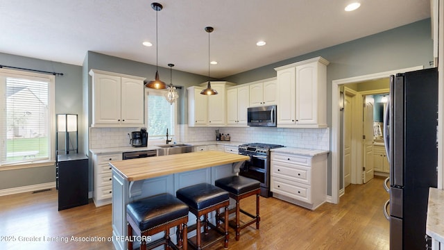 kitchen featuring a sink, tasteful backsplash, light wood finished floors, white cabinetry, and appliances with stainless steel finishes