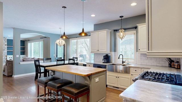 kitchen with butcher block countertops, a sink, a kitchen breakfast bar, backsplash, and white cabinets