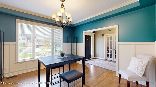 dining area featuring a decorative wall, an inviting chandelier, visible vents, and a wainscoted wall