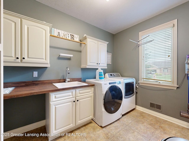 washroom with a sink, cabinet space, visible vents, washer and dryer, and light tile patterned floors