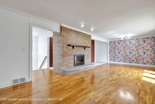 unfurnished living room with wood finished floors, ornamental molding, visible vents, a brick fireplace, and baseboards
