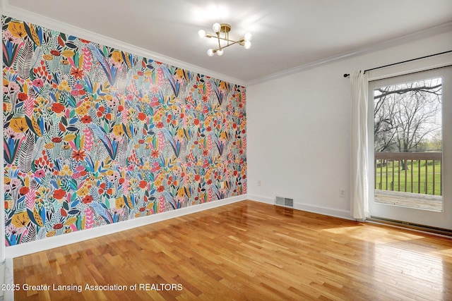 spare room with wood finished floors, a notable chandelier, visible vents, baseboards, and ornamental molding