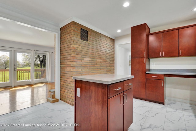kitchen with light countertops, reddish brown cabinets, marble finish floor, and brick wall