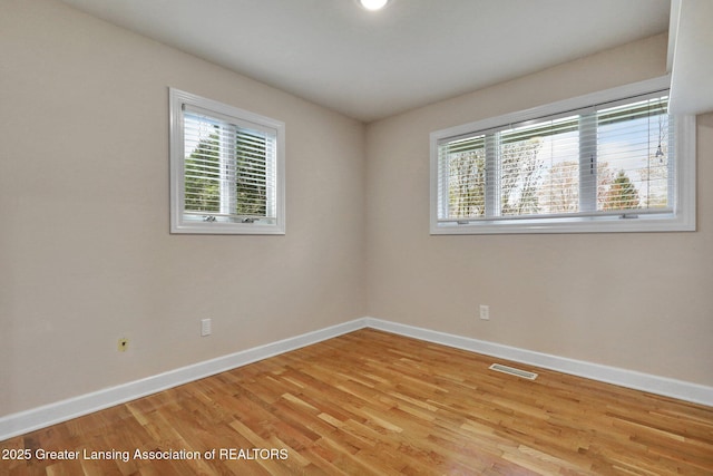 empty room featuring light wood-style flooring, plenty of natural light, baseboards, and visible vents