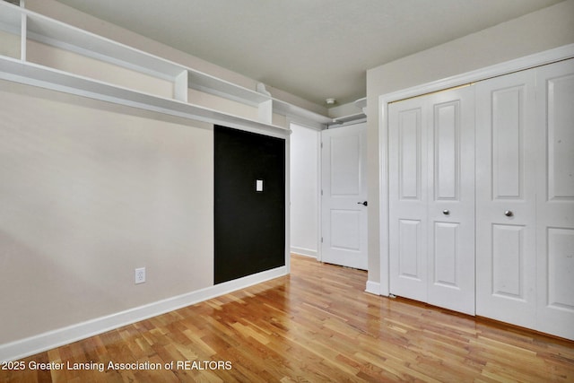 unfurnished bedroom featuring baseboards, light wood finished floors, and a closet