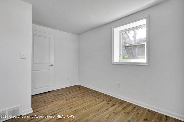 empty room featuring visible vents, wood finished floors, and baseboards