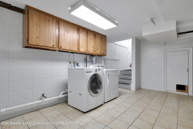 washroom featuring tile walls, separate washer and dryer, light tile patterned flooring, and cabinet space