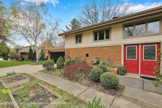 view of front facade with concrete driveway, a vegetable garden, brick siding, and a garage