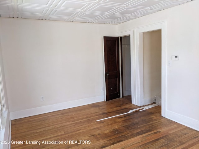 empty room featuring wood finished floors, baseboards, and an ornate ceiling