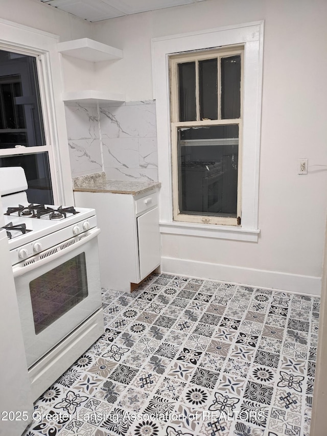 kitchen featuring white gas range, open shelves, backsplash, light countertops, and white cabinets