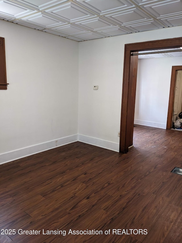 unfurnished room featuring baseboards, an ornate ceiling, and dark wood finished floors