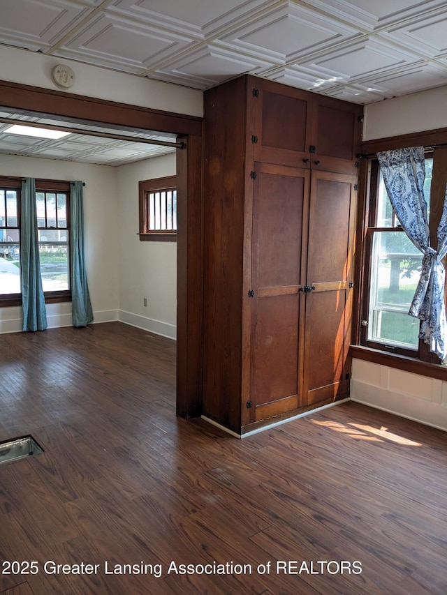 unfurnished room featuring baseboards, dark wood-type flooring, and plenty of natural light