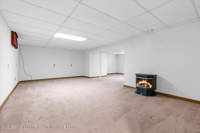 finished below grade area with carpet flooring, a paneled ceiling, baseboards, and a wood stove