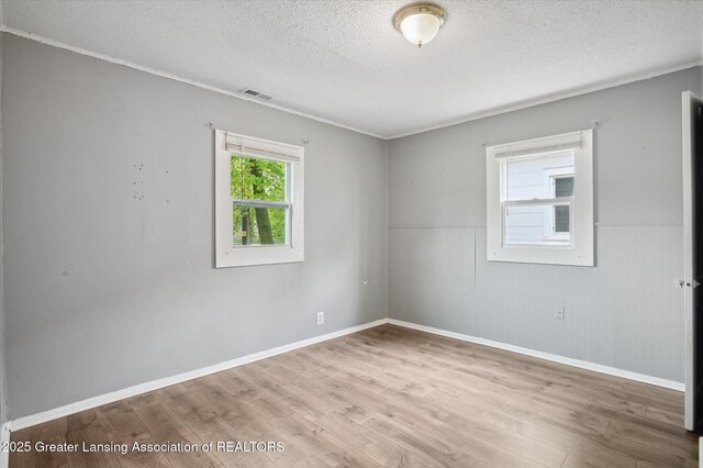 1406 N Martin Luther King Jr Blvd, Lansing, MI 48915 - spare room featuring a textured ceiling, baseboards, visible vents, a wainscoted wall, and wood finished floors
