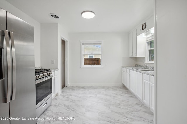 900 Holten St, Lansing, MI 48915 - kitchen featuring appliances with stainless steel finishes, a sink, white cabinets, baseboards, and light marble finish floors