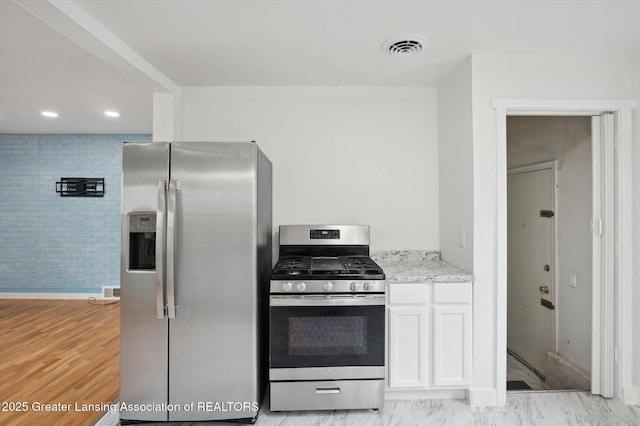 900 Holten St, Lansing, MI 48915 - kitchen featuring appliances with stainless steel finishes, light stone countertops, white cabinets, baseboards, and light wood-type flooring