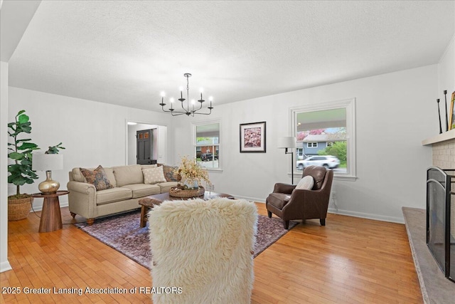 living room with a textured ceiling, a fireplace with raised hearth, an inviting chandelier, baseboards, and light wood-style floors