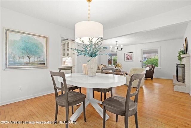 dining room featuring an inviting chandelier, light wood-style flooring, a brick fireplace, and baseboards