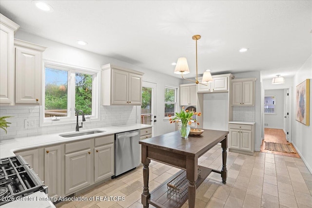 kitchen with pendant lighting, stainless steel dishwasher, a sink, backsplash, and light countertops