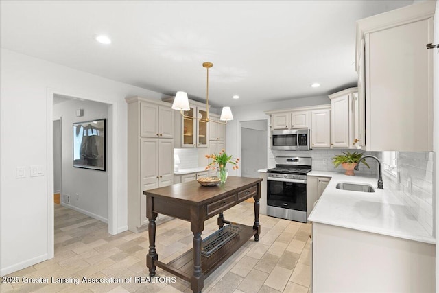 kitchen with a sink, pendant lighting, backsplash, light countertops, and appliances with stainless steel finishes